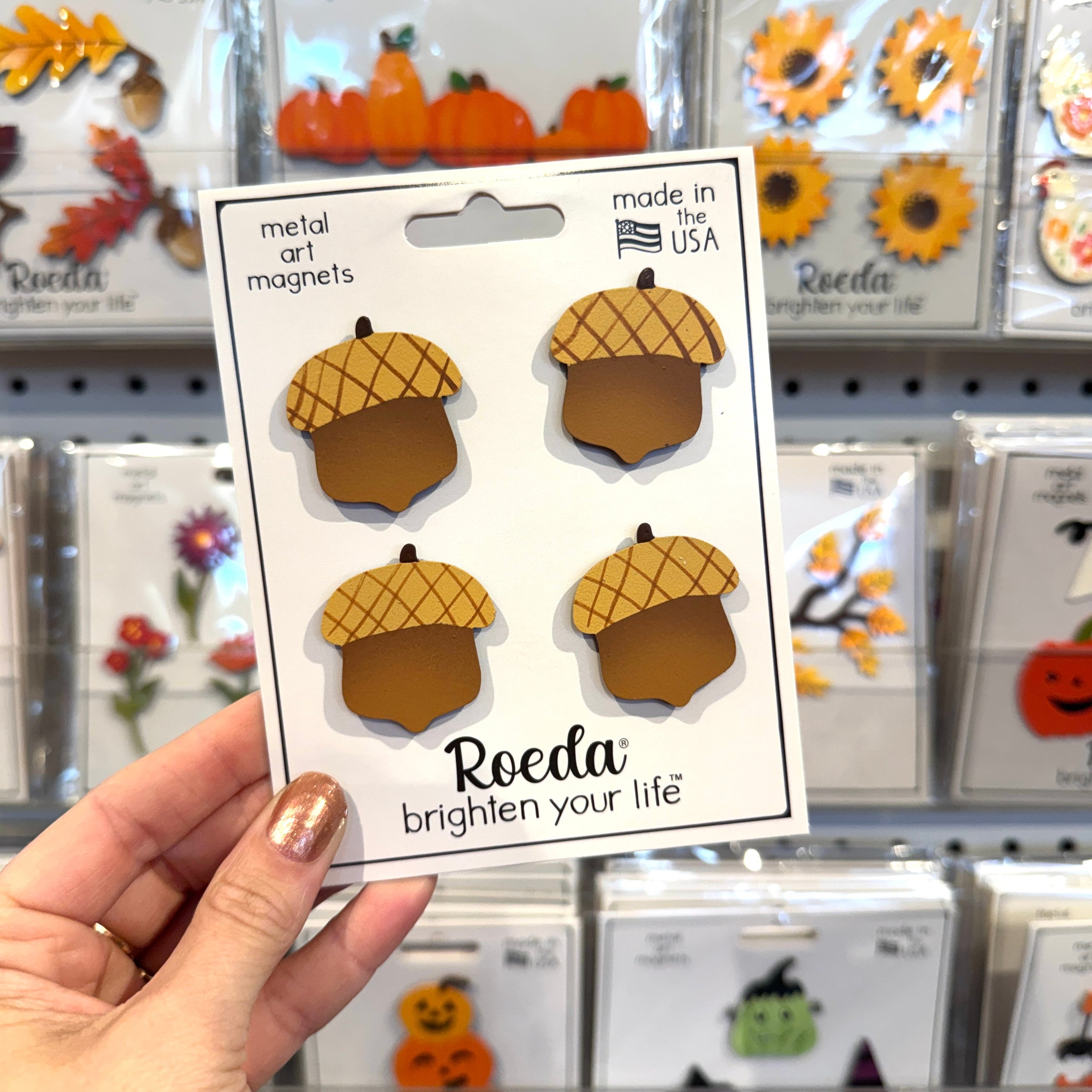 Hand holding a package of acorn-shaped metal art magnets with &