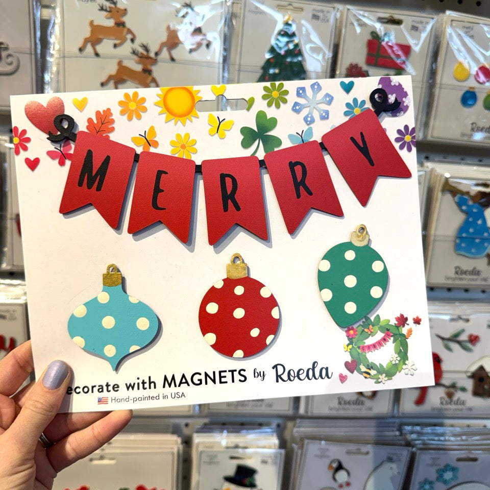 A hand holds a white card featuring a Christmas-themed magnet banner with red pennants spelling &