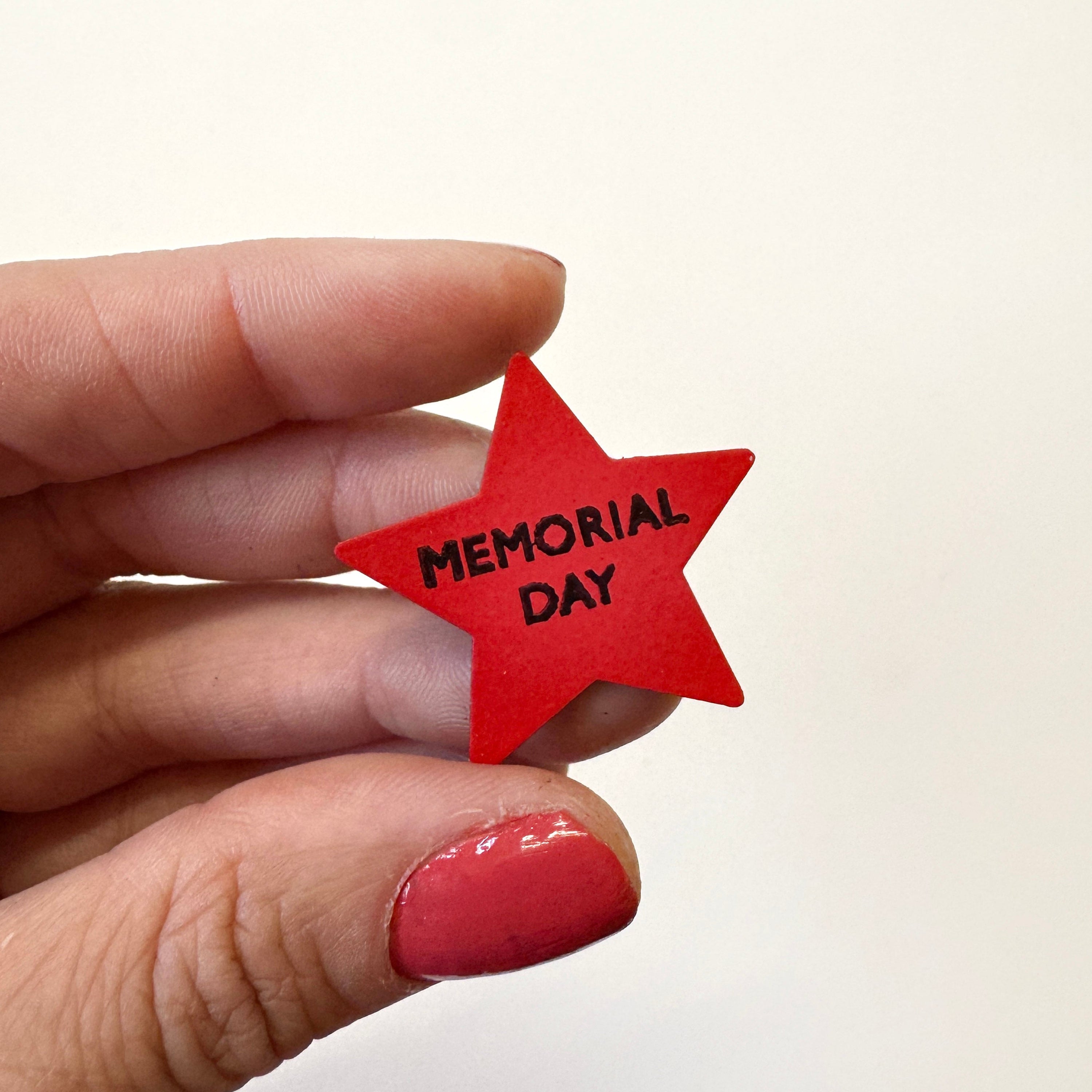 A hand with red nail polish holds a small red star-shaped magnet with the words &