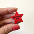 A hand with red nail polish holds a small red star-shaped magnet with the words &