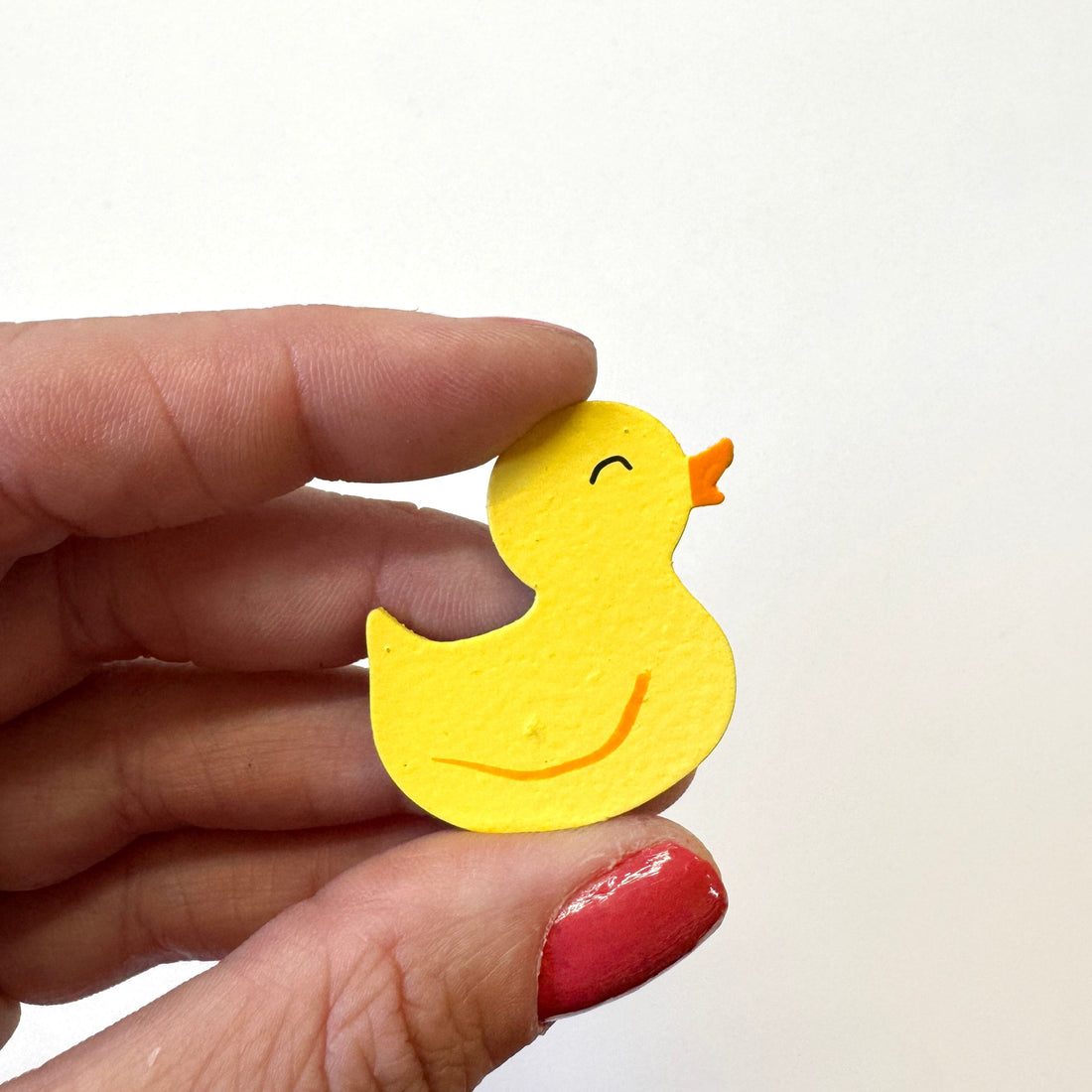 A small yellow rubber duck magnet held between a person&