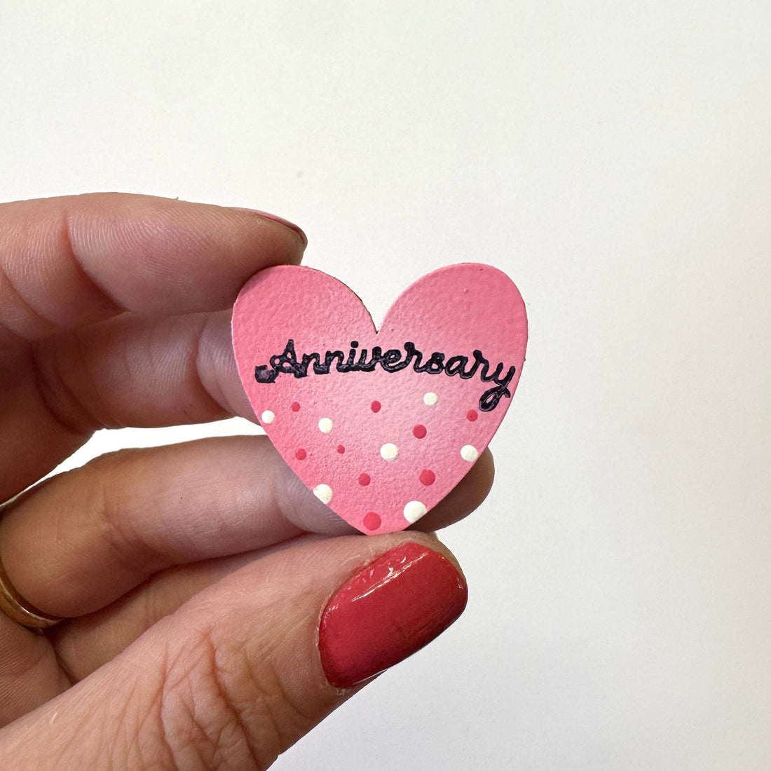 A hand holds a small pink heart-shaped magnet that reads &