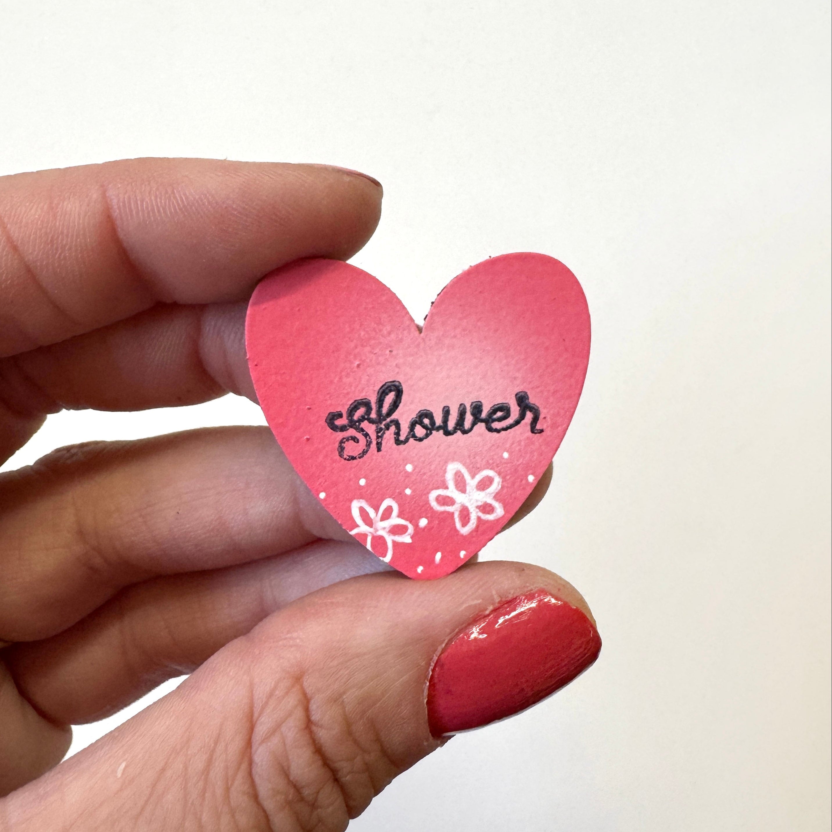 A hand  holds a small pink heart-shaped magnet that says &