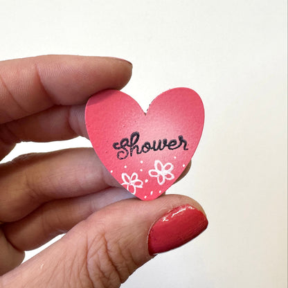 A hand  holds a small pink heart-shaped magnet that says &