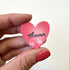 A hand  holds a small pink heart-shaped magnet that says &