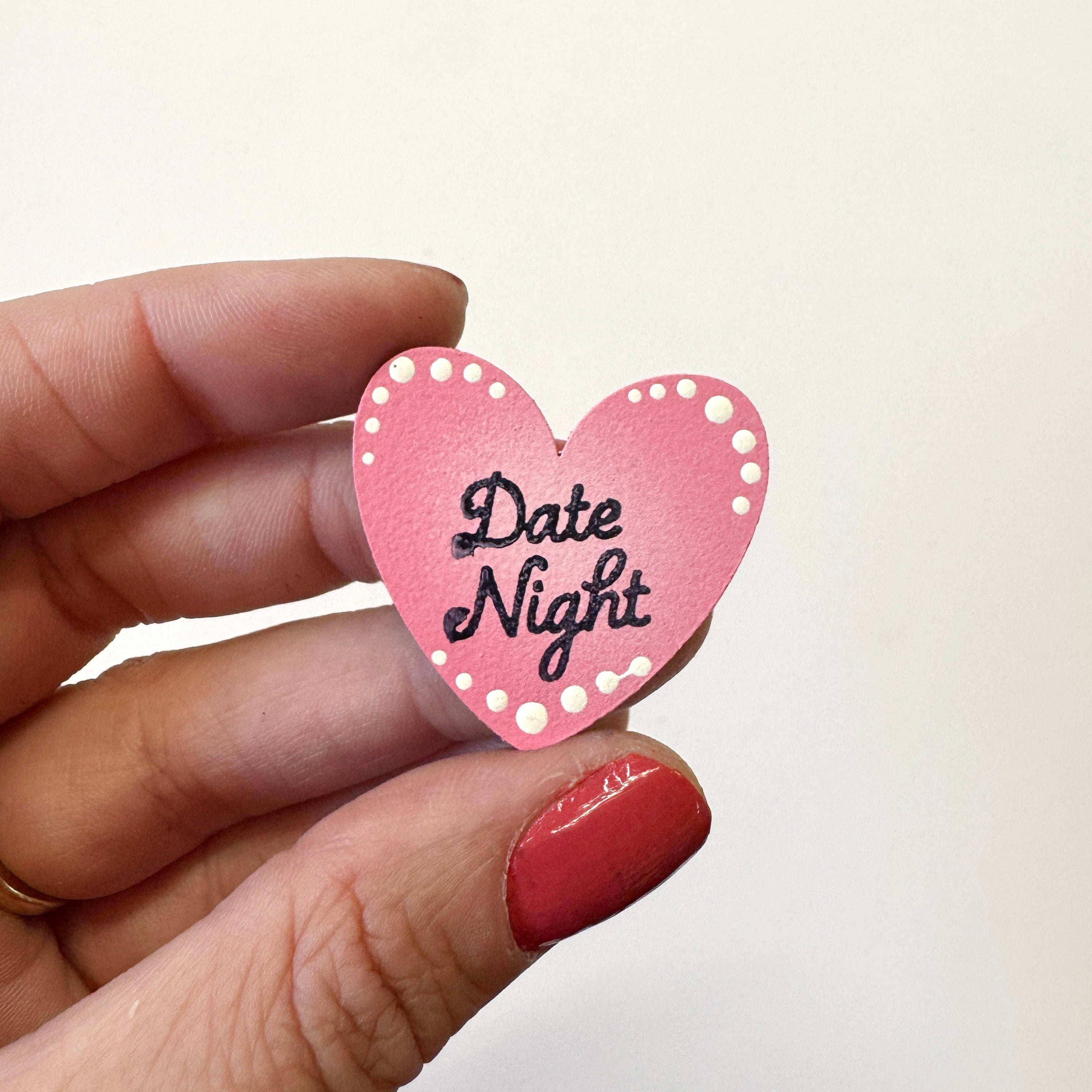 A hand holds a small pink heart-shaped magnet that reads &