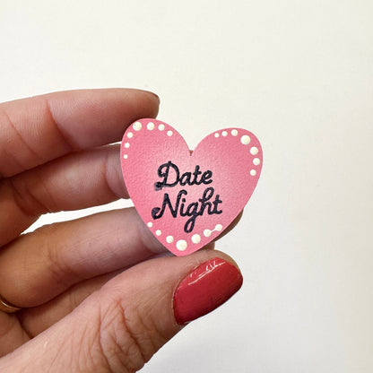 A hand holds a small pink heart-shaped magnet that reads &
