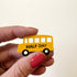 A hand holds a small yellow school bus magnet with the words &