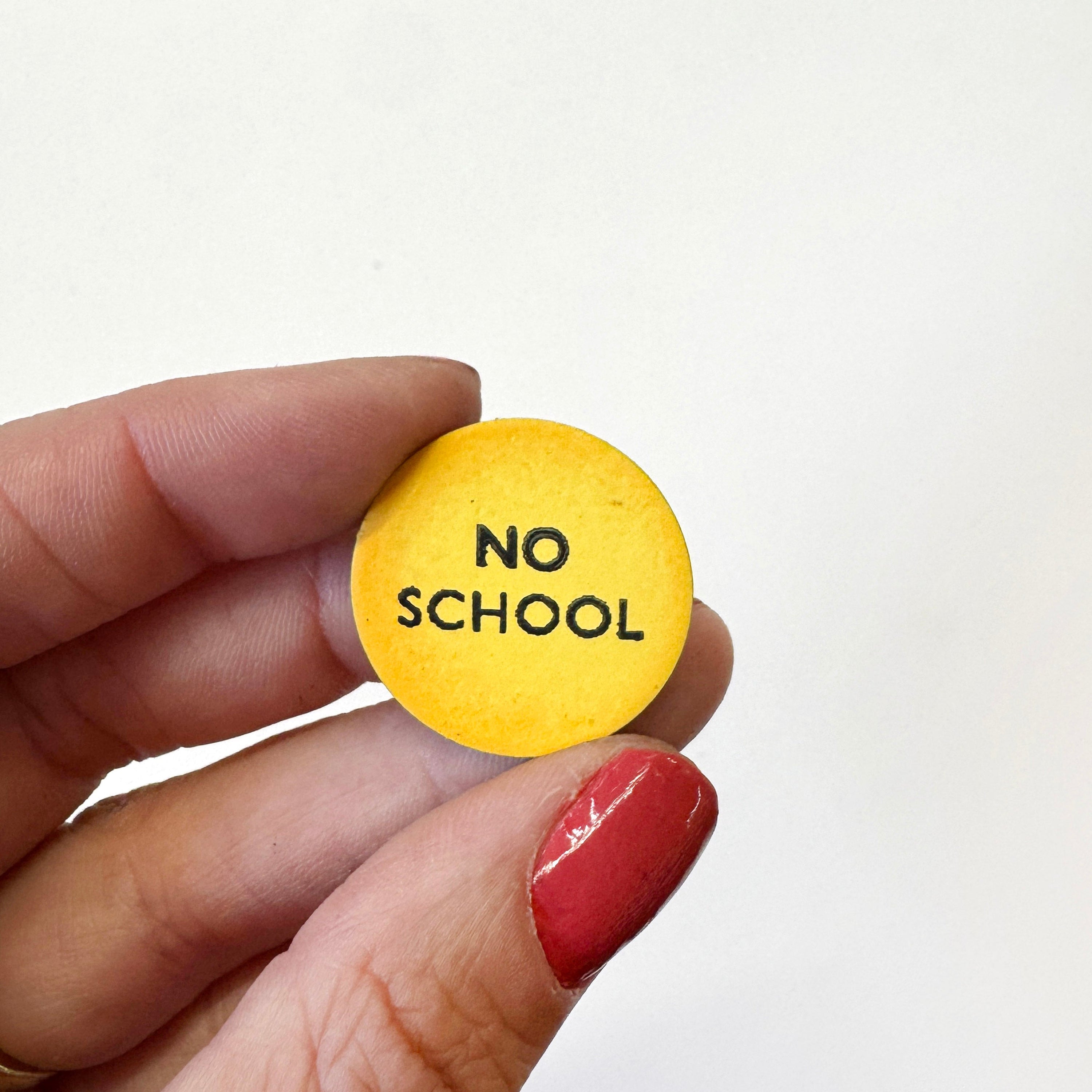 A hand holds a small round yellow magnet that reads &