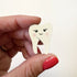 A hand with red nail polish holds a small, cute, tooth-shaped magnet with a smiling face against a plain white background.