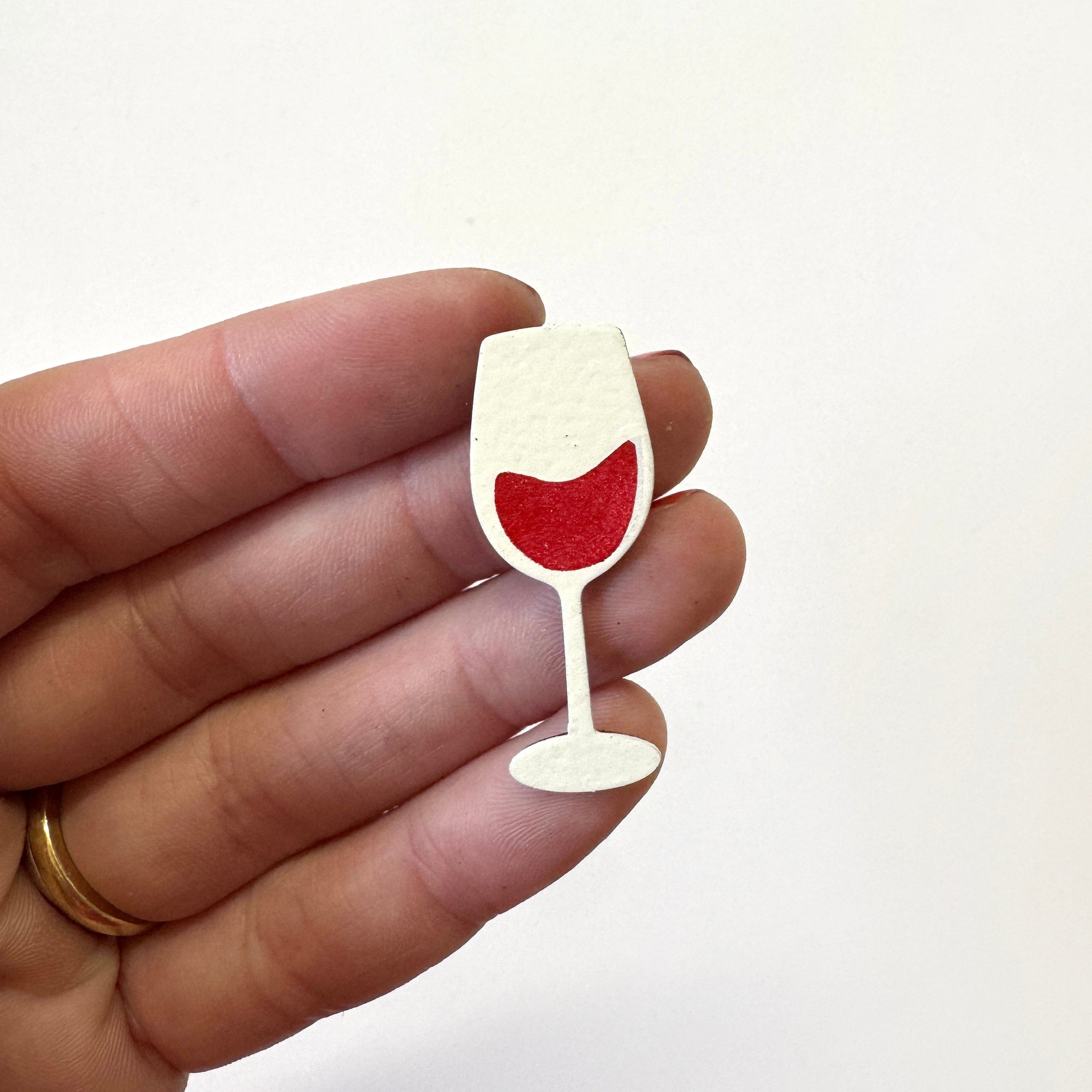 A hand holding a small, wine glass-shaped magnet 
