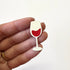 A hand holding a small, wine glass-shaped magnet 