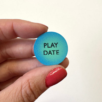 A hand holds a round blue magnet that reads &